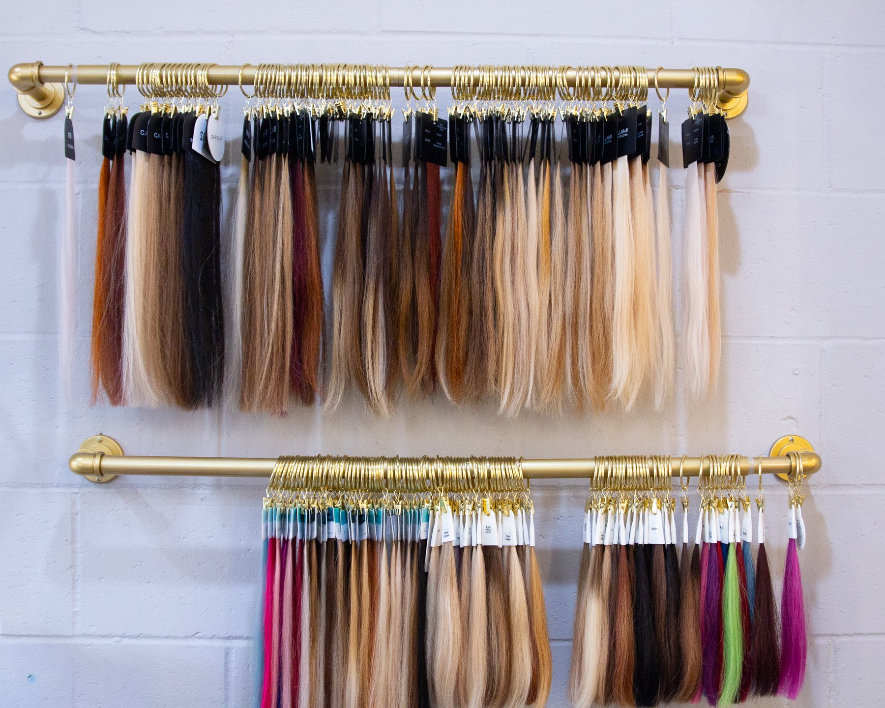 Rows of hair colour swatches hanging from brass rods on a white brick wall.