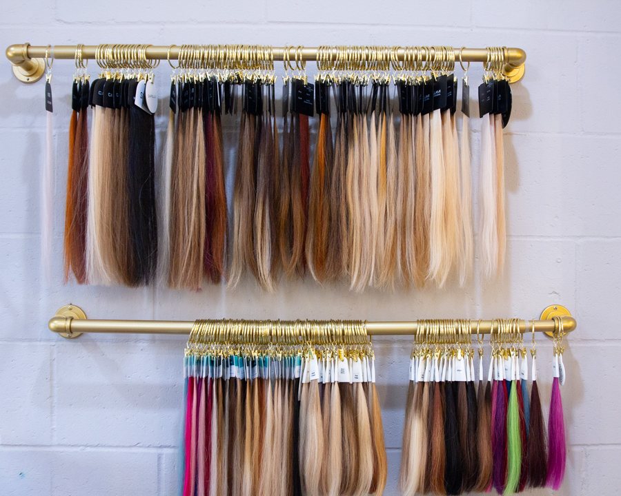Rows of hair colour swatches hanging from brass rods on a white brick wall.